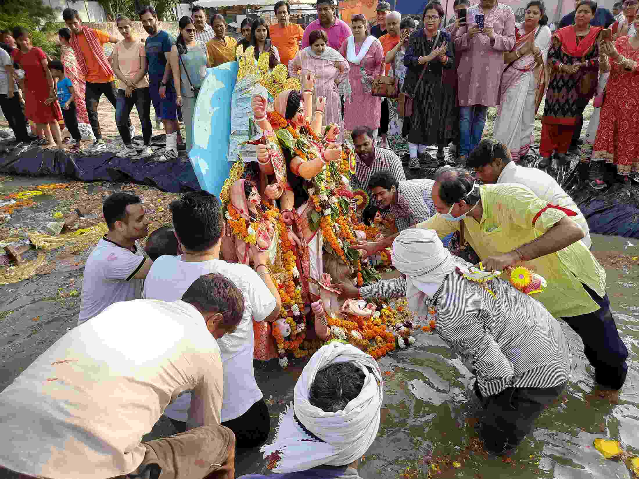 People stand on the edges of an artificial pond, watching as a group of men prepare to lower a colourful idol of the Goddess Durga, laden with flowers, into the pond water